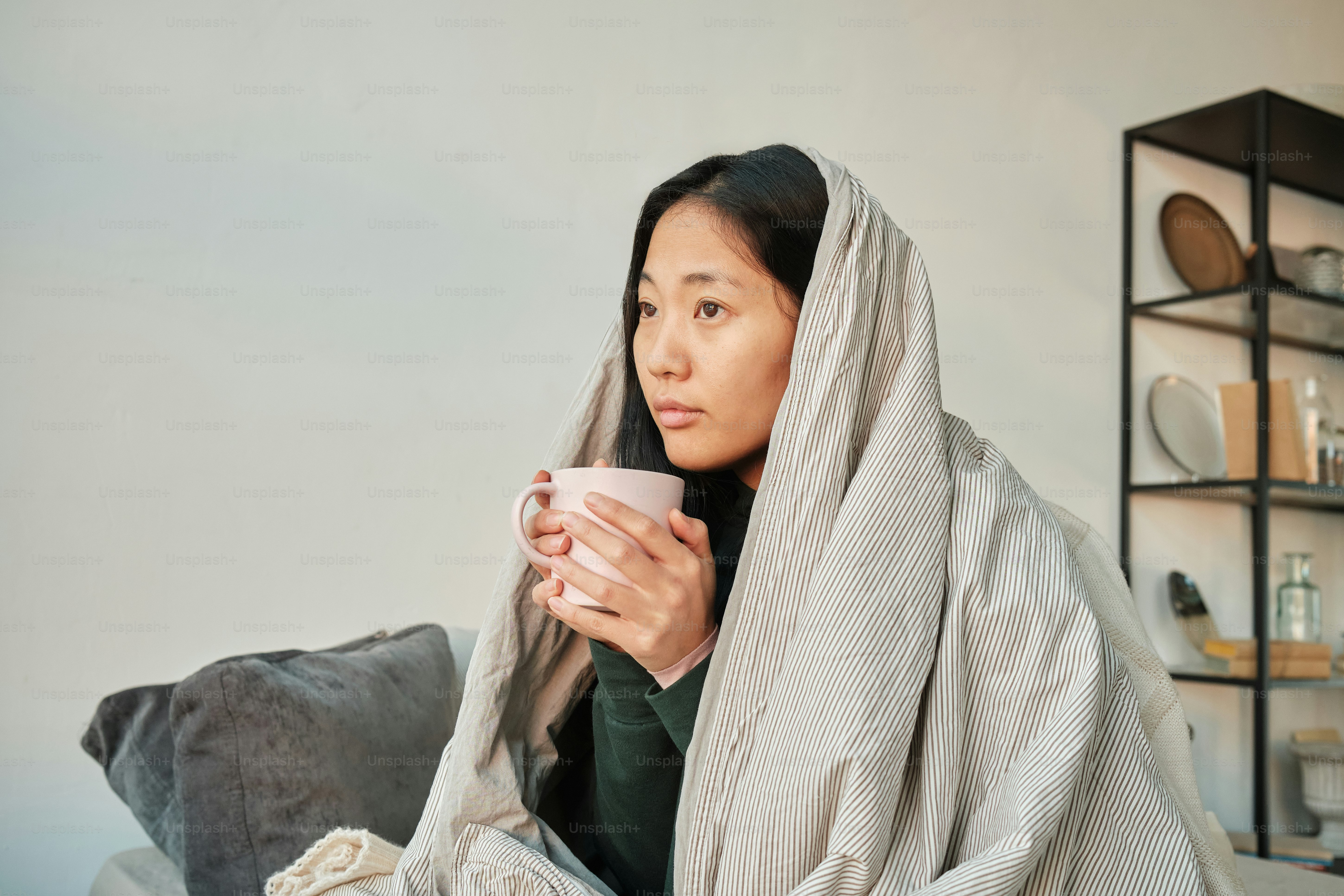 asian girl with a mug sitting on a bed wrapped in a blanket